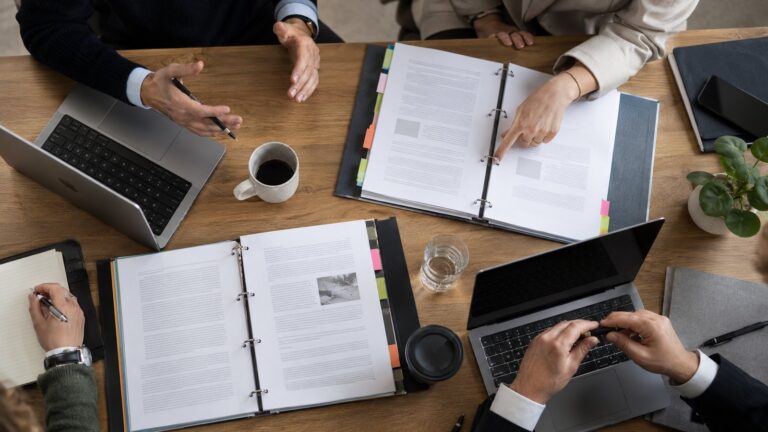 Overhead view of an audit team working through binders and laptops at a meeting table